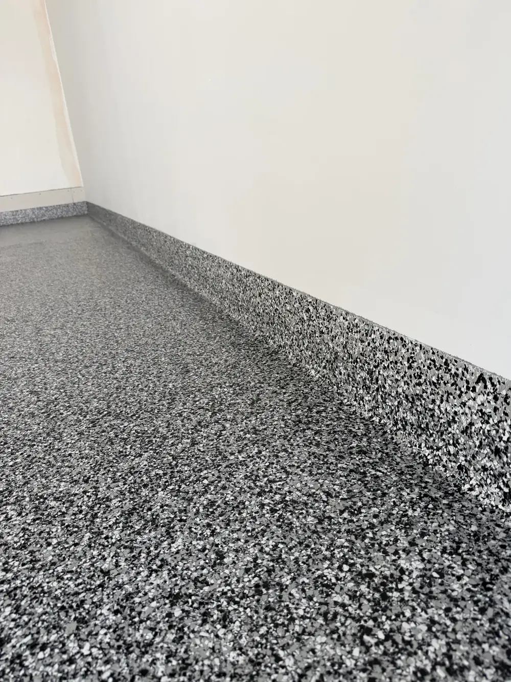 Close-up of gray full-flake coating carried up a garage stem wall, installed by Iron Cross