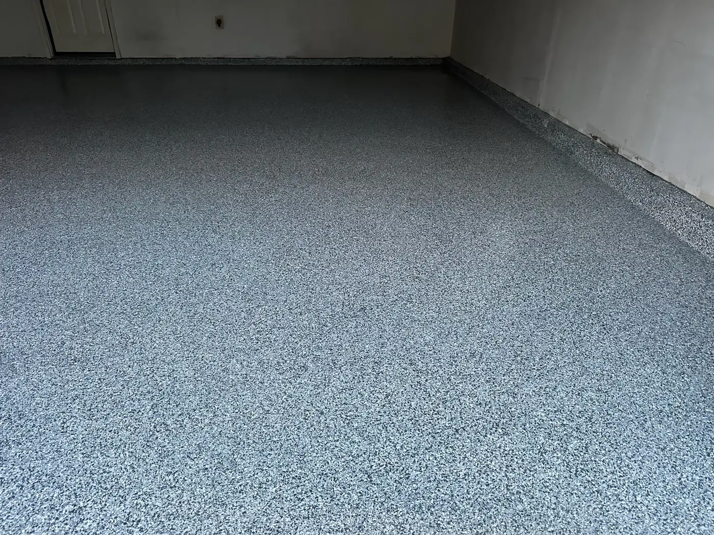Gray and blue full-flake garage floor with a coated stem wall, installed by Iron Cross Coatings